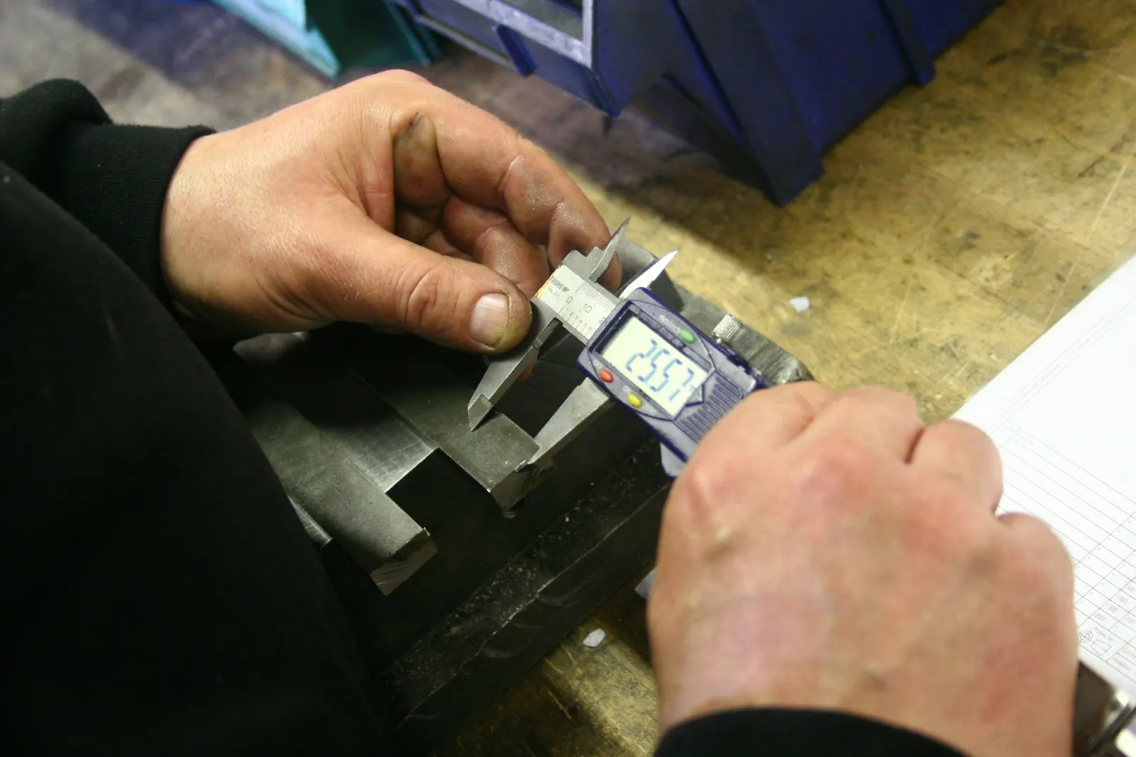 Manos midiendo una pieza con un calibrador digital; fotografía de referencia de inspección.